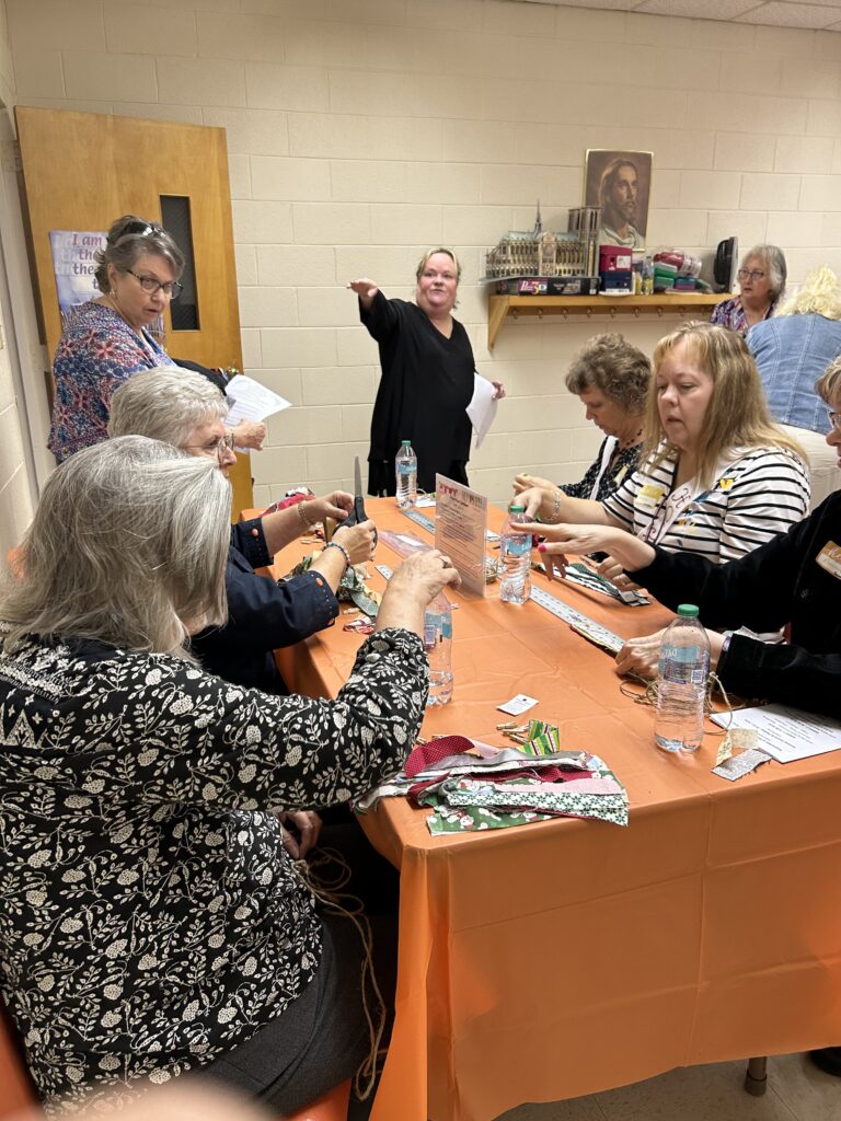 Christie Kelly instructing participants on how to make a cloth prayer garland during a craft session.